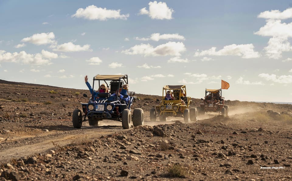 Drei offene Buggys wirbeln auf einer steinigen Piste Staub auf, darüber verstreute weiße Wolken