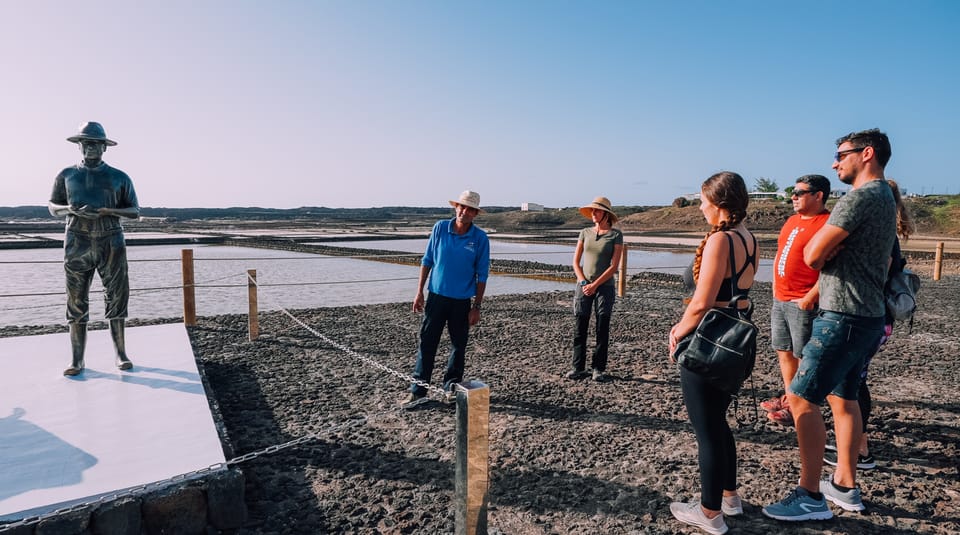Guide and visitors beside salt pans and a statue of a salt worker