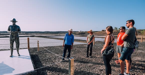 Guide and visitors beside salt pans and a statue of a salt worker