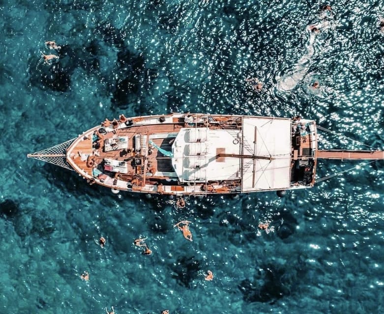 A wooden excursion boat anchored beside pale cliffs above clear turquoise Aegean water