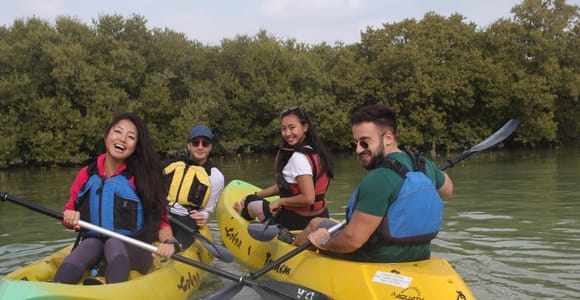 A yellow kayak moving through a narrow channel between green mangroves in northern Qatar