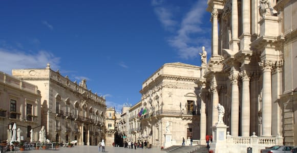 Baroque cathedral façade and palazzi on a wide square under a blue sky in Syracuse
