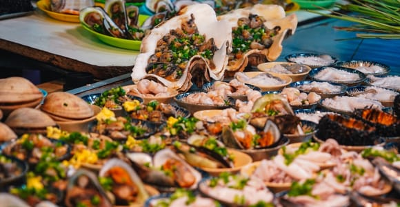 Night market stall lit by bare bulbs with trays of crab and prawns on crushed ice, a vendor leaning over the counter