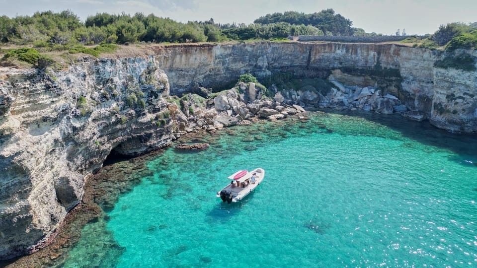 Small motorboat in a turquoise cove below pale limestone cliffs