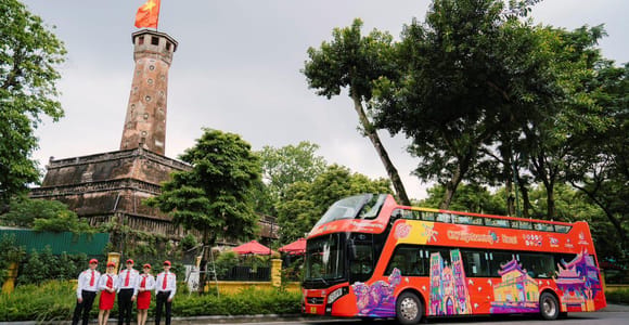 A red bridge crosses green water beside trees and old buildings at Hoan Kiem Lake