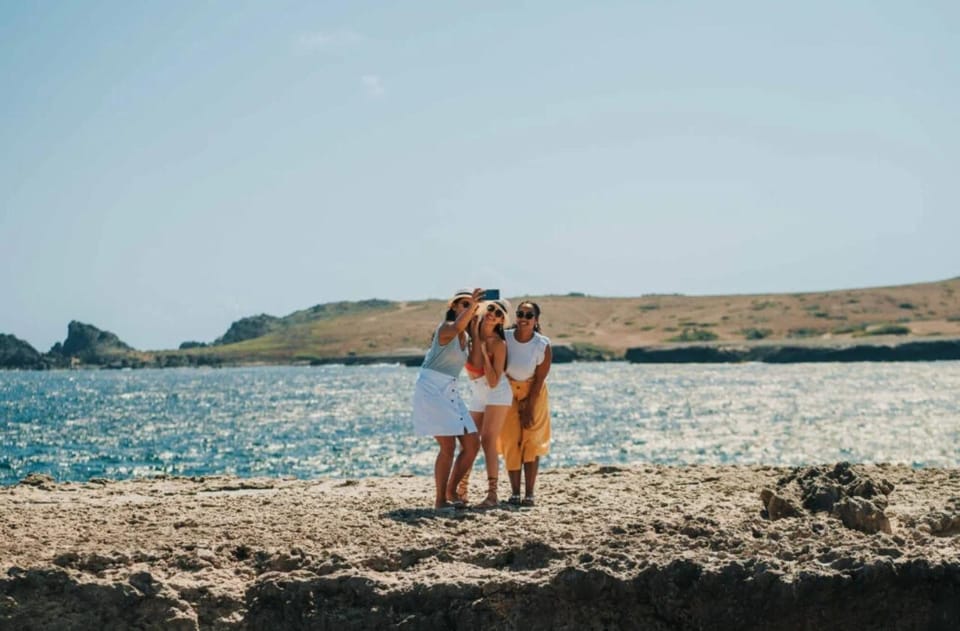 Three women taking a selfie on a rocky shore, with sea and a dry coastline behind them