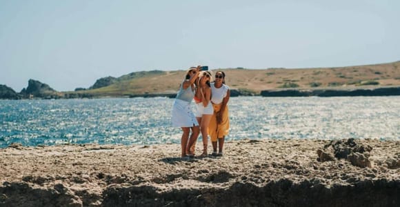 Three women taking a selfie on a rocky shore, with sea and a dry coastline behind them