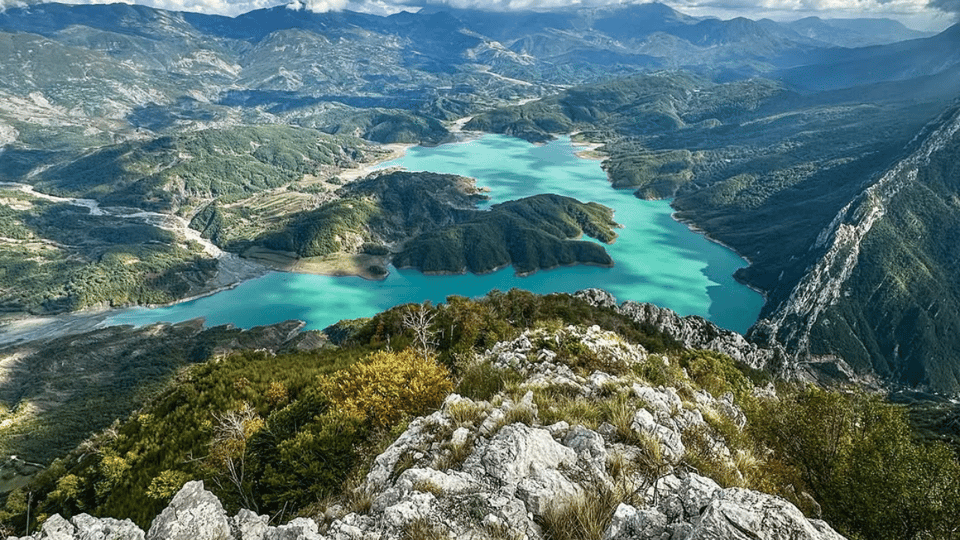 Turquoise Bovilla Lake winding between steep green-grey mountains below Gamti