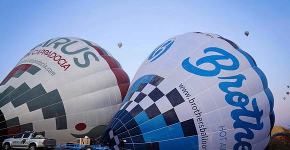 Two hot-air balloon envelopes being inflated on the ground at a Cappadocia launch site before sunrise