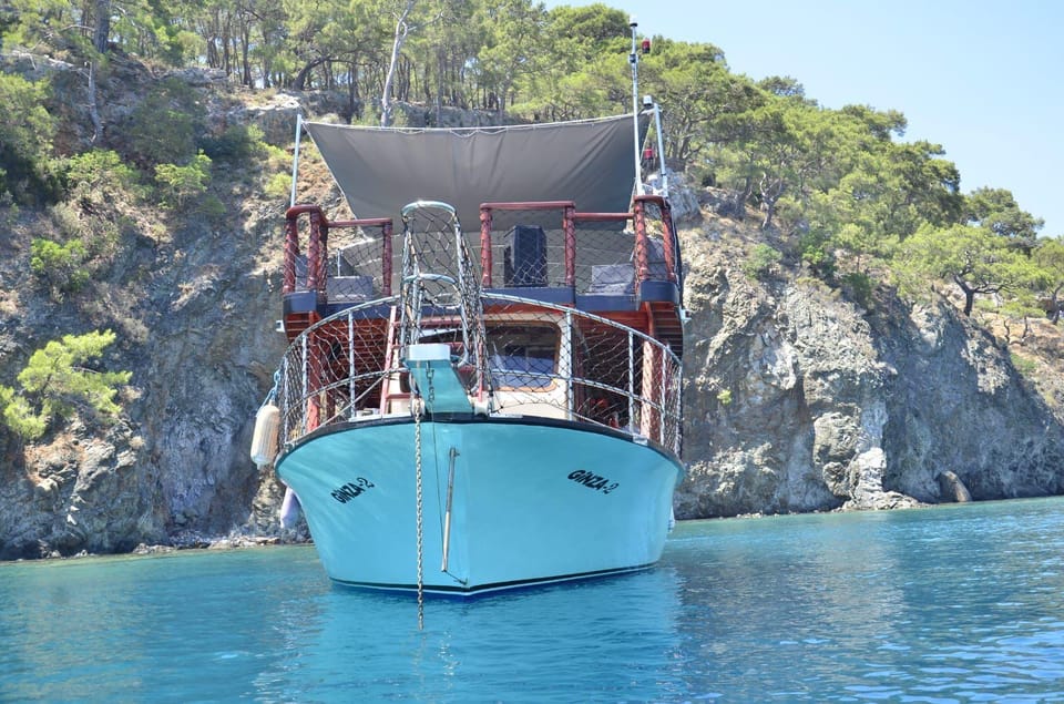 Turquoise wooden gulet anchored in a calm bay below a rocky, pine-covered shore