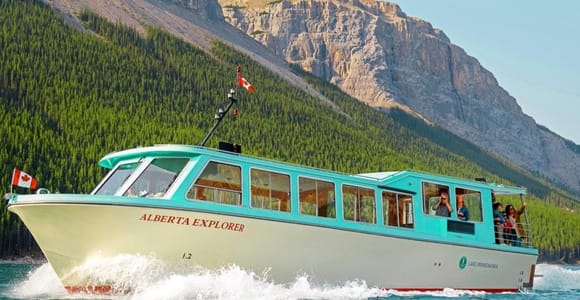 Tour boat crossing a deep blue mountain lake beneath forested slopes and pale rocky peaks