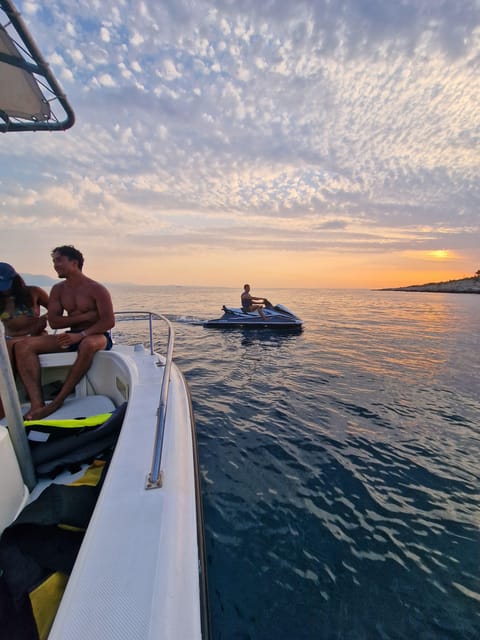 Sunset sky and calm sea seen from the deck of a boat, with a jet ski and a rocky shore in the distance