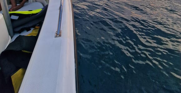 Sunset sky and calm sea seen from the deck of a boat, with a jet ski and a rocky shore in the distance