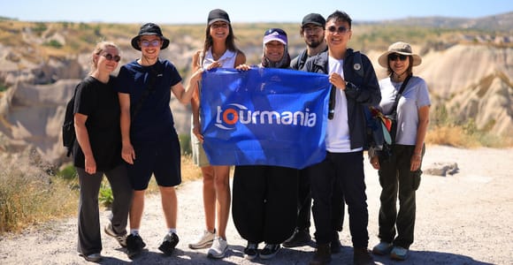 A small group of visitors holding a banner at a viewpoint above a pale, eroded Cappadocia valley