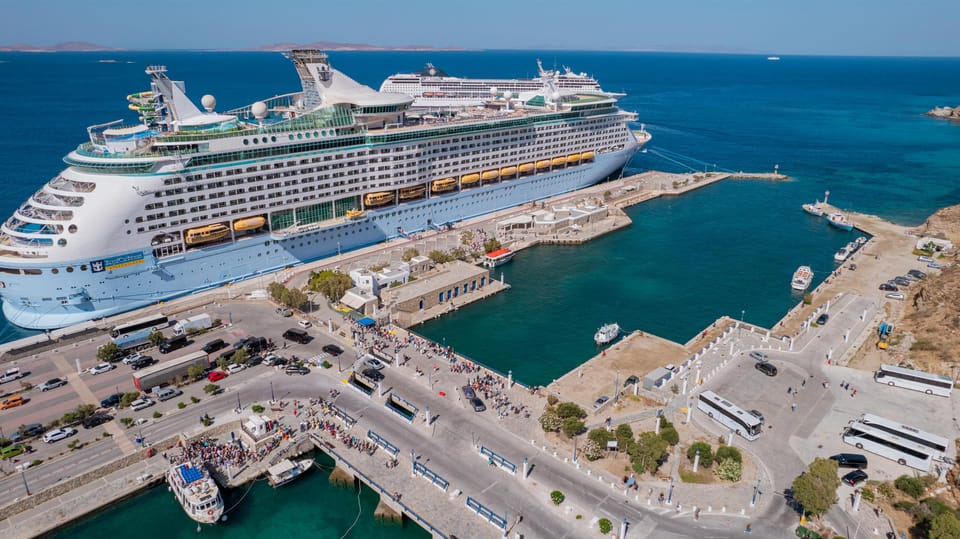 Aerial view of a large cruise ship moored at a Mykonos quay, with coaches and small ferries on the neighbouring jetties