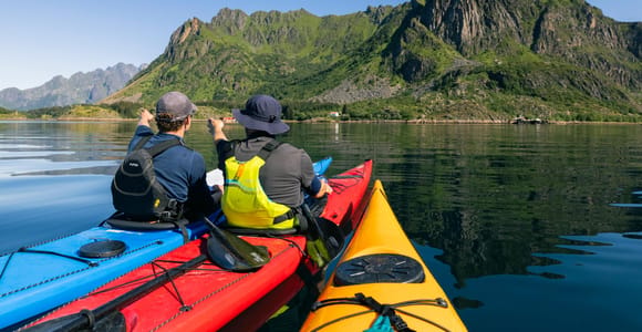 Two sea kayaks on clear water with steep Lofoten mountains behind