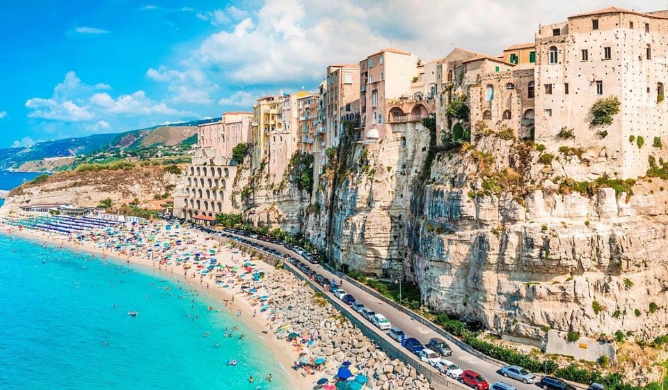 Tropea on the cliff edge above a beach with parasols and the coast road below