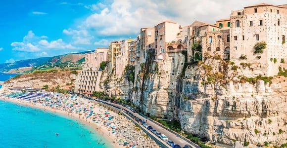 Tropea on the cliff edge above a beach with parasols and the coast road below