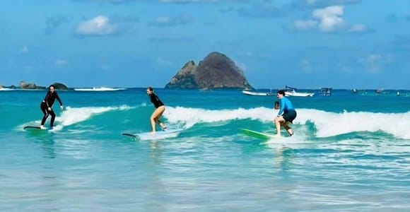 A beginner surfer carrying a board across a broad sandy beach