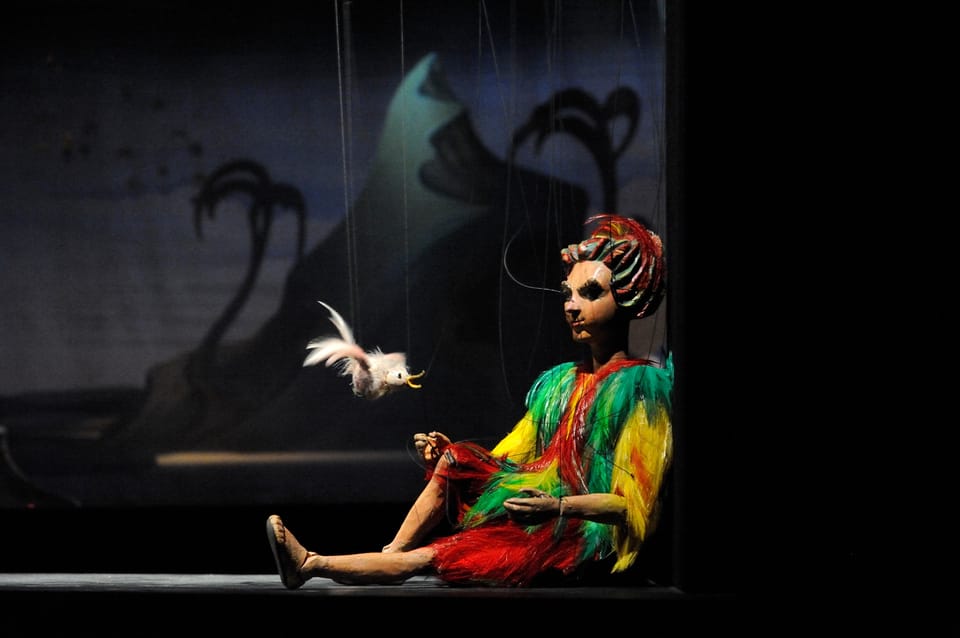 Wooden marionettes in embroidered costumes hanging on strings against a painted stage backdrop