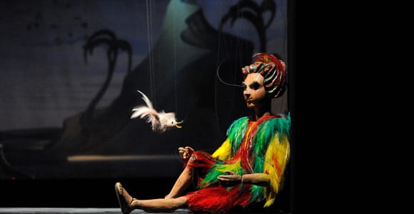 Wooden marionettes in embroidered costumes hanging on strings against a painted stage backdrop