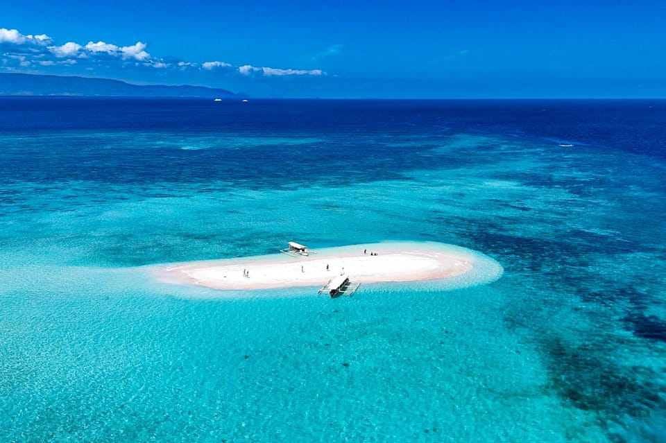 A white sandbar in turquoise water with two small wooden boats moored beside it