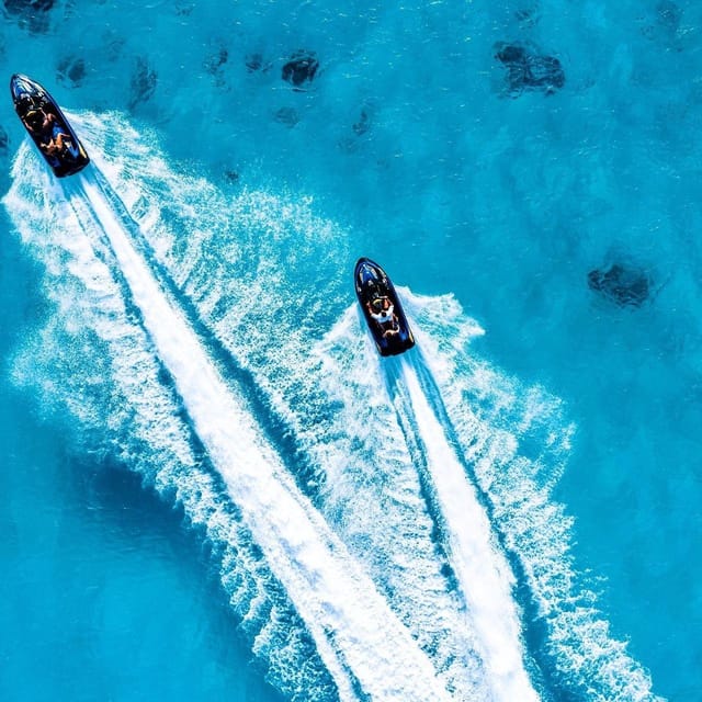 Two jet skis photographed from directly above, cutting long parallel white wakes across bright blue water