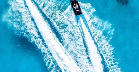 Two jet skis photographed from directly above, cutting long parallel white wakes across bright blue water