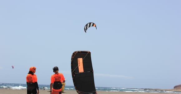 A kite canopy above choppy blue water off a broad sandy bay