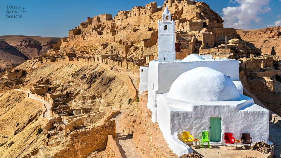 A hillside Berber village of sand-coloured stone houses above a whitewashed mosque with a minaret and green door
