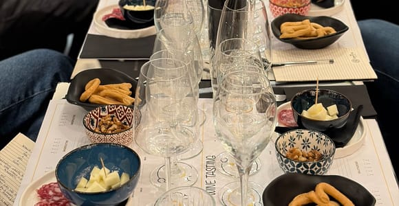 A long tasting table set with rows of wine glasses and small bowls of cheese, salami and taralli