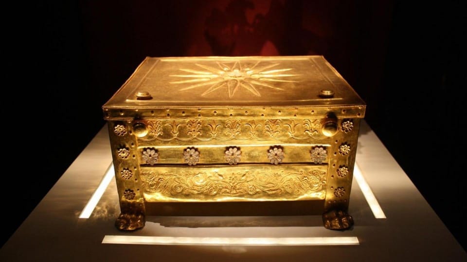 A gold chest with a star-shaped sunburst on its lid, lit in a dark museum display