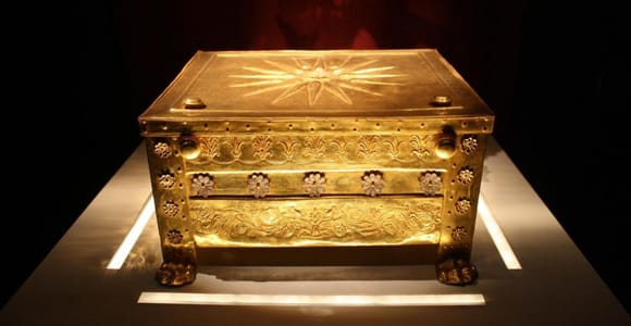A gold chest with a star-shaped sunburst on its lid, lit in a dark museum display