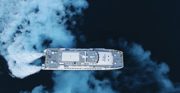A white passenger catamaran seen from directly above, leaving a foaming wake across dark blue water