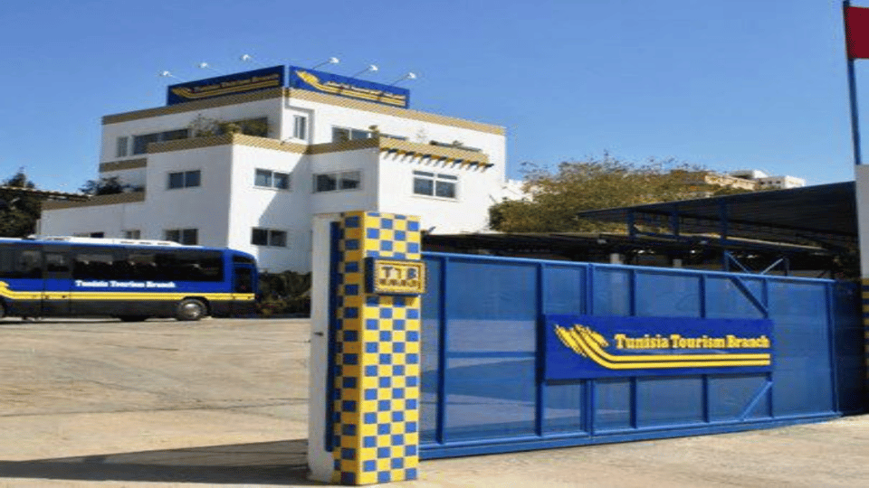 A white passenger car waiting beside an airport terminal with suitcases by the rear door