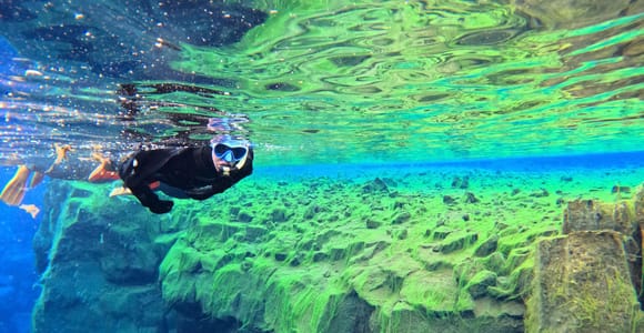 A snorkeller floating above clear blue rock walls in the Silfra fissure
