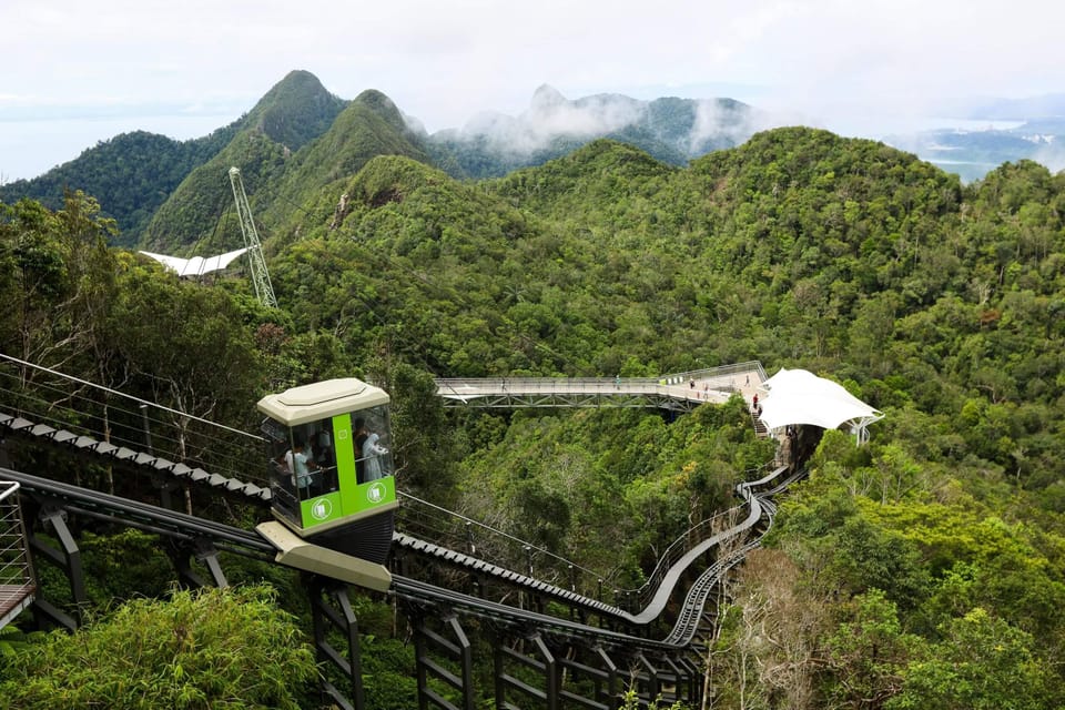 Green inclined lift car climbing a steel rack track above rainforest, with the curved Sky Bridge walkway and mist-covered limestone peaks behind