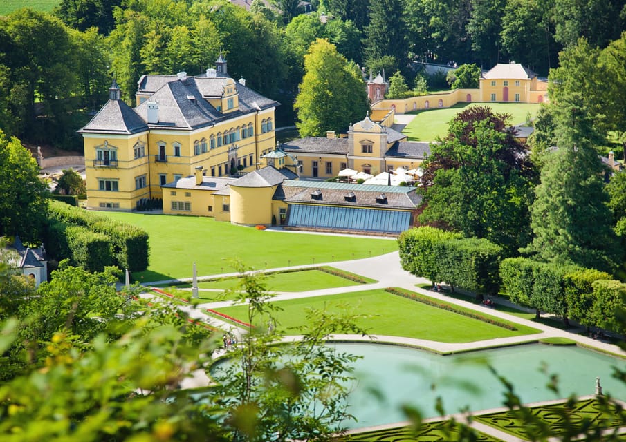 A formal garden with a pale yellow Baroque palace behind a gravel path and clipped hedges