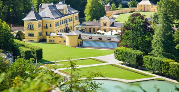 A formal garden with a pale yellow Baroque palace behind a gravel path and clipped hedges