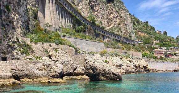 Turquoise water in front of a rocky coast with a road on high retaining walls above it