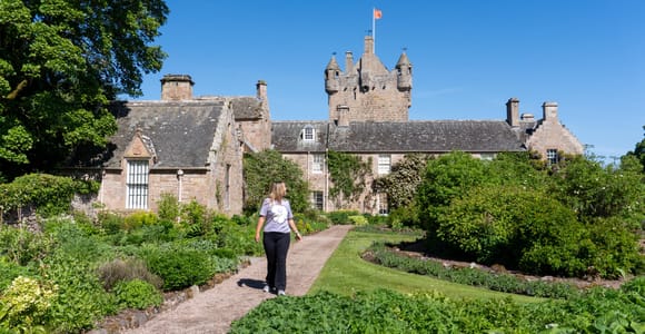 A stone Highland castle framed by mature trees and formal green gardens