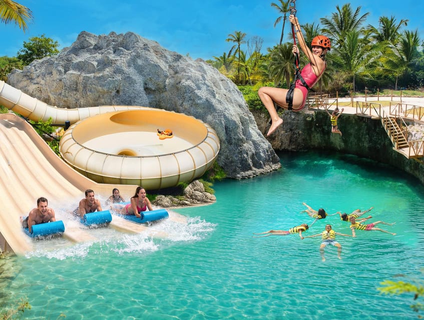 Water park with a curving slide running into a turquoise pool, a person on a zip line overhead and children floating in yellow life jackets below
