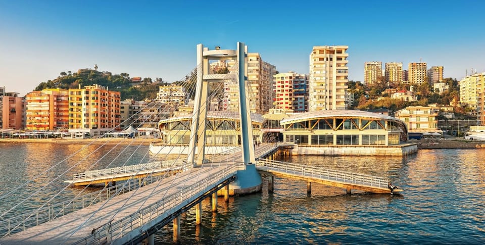 Pedestrian bridge with a tall pylon over the water, apartment blocks and a wooded hill behind
