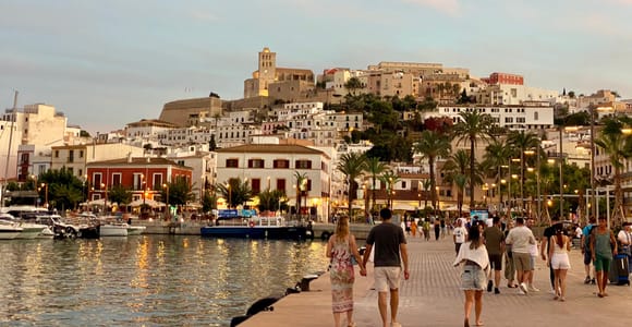 Ibiza Town old town on its hill above the harbour at dusk, with the cathedral tower and people strolling along the quay
