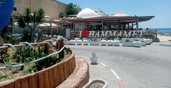 Sand-coloured medina ramparts beside a seafront café with an "I love Hammamet" sign, white domes and the open sea behind