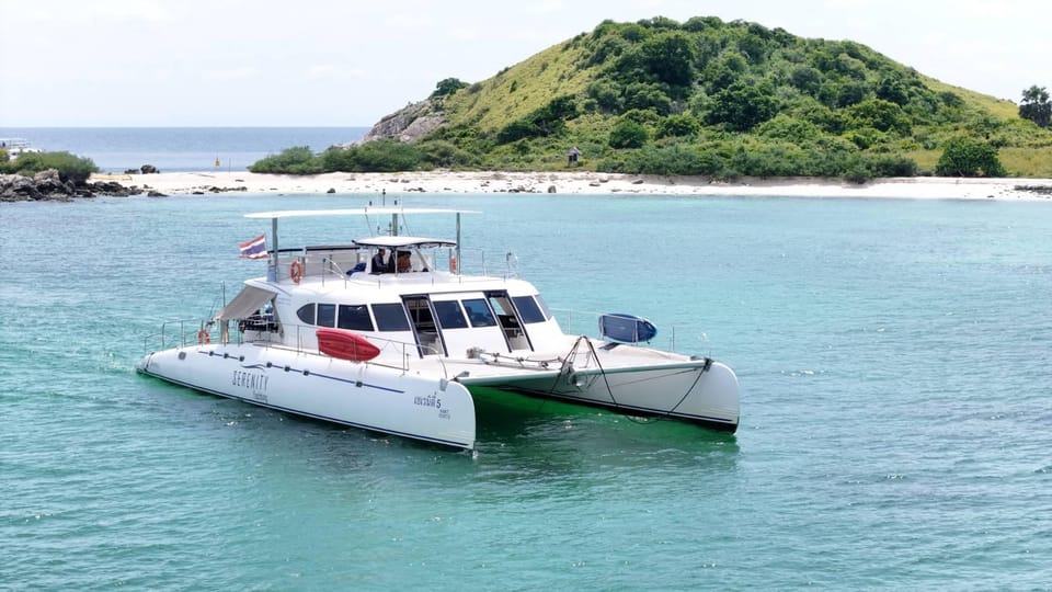 A broad white catamaran anchored in clear water near a wooded Thai island