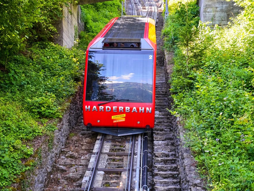 Red funicular car on a steep track between green slopes and a stone stairway