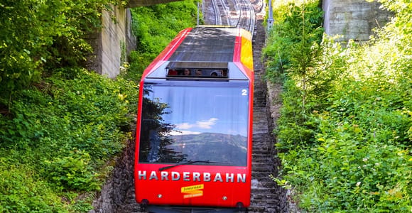 Red funicular car on a steep track between green slopes and a stone stairway