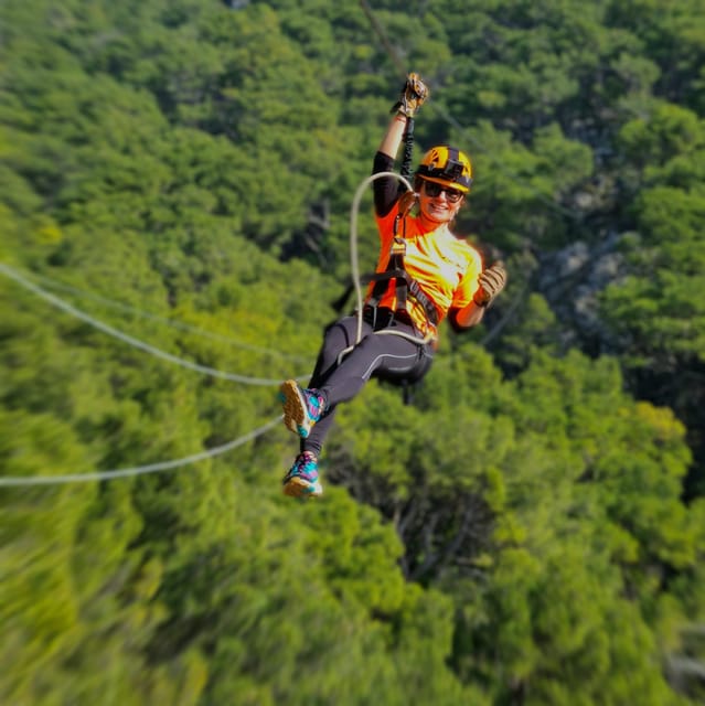 A person in a helmet and harness sliding along a steel cable above a wooded canyon
