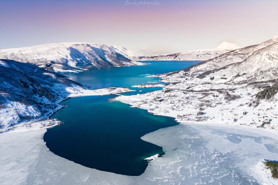 Snow-covered mountains descending towards a dark Norwegian fjord near Narvik